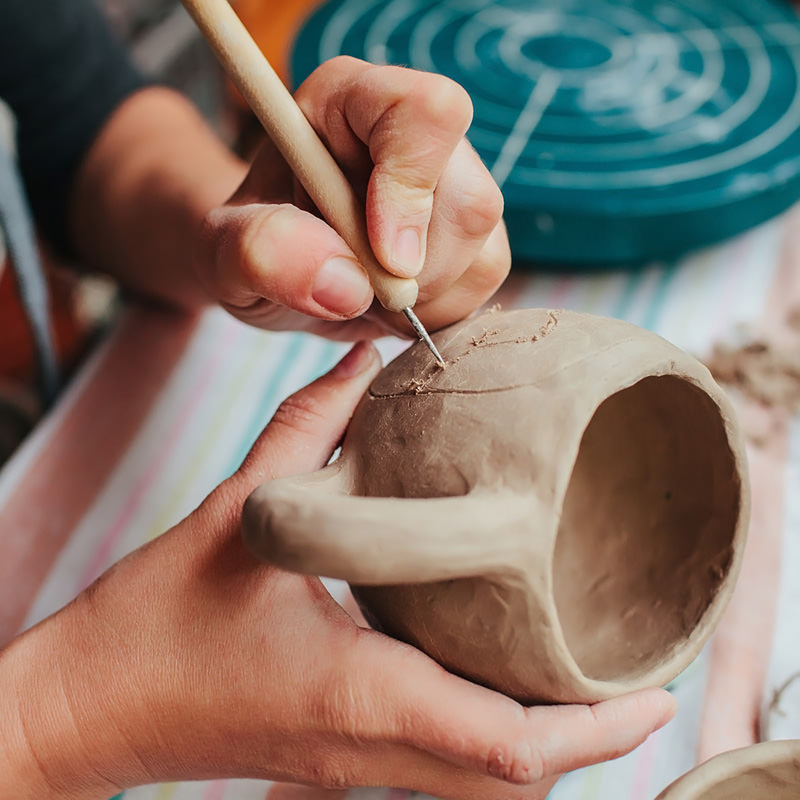 Woman potter making pattern on the ceramic cup in her workshop.