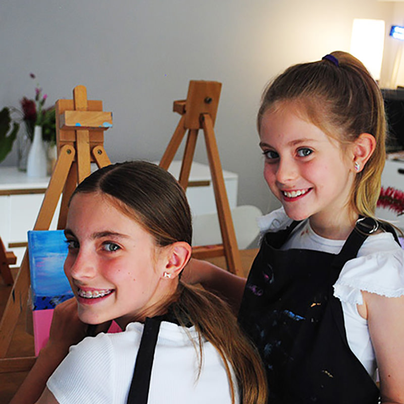 Smiling happy teenage and young girls standing at easels