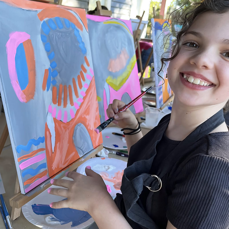 happy young girl painting with bright colours an abstract style on easel at table