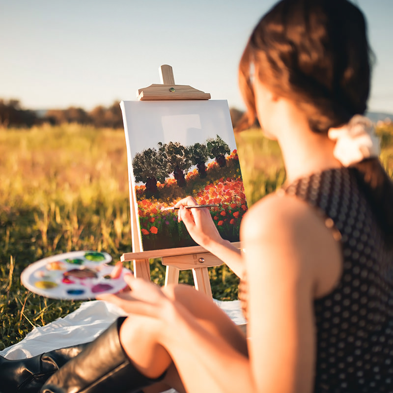 Happy girl painting outdoors on canvas at sunset