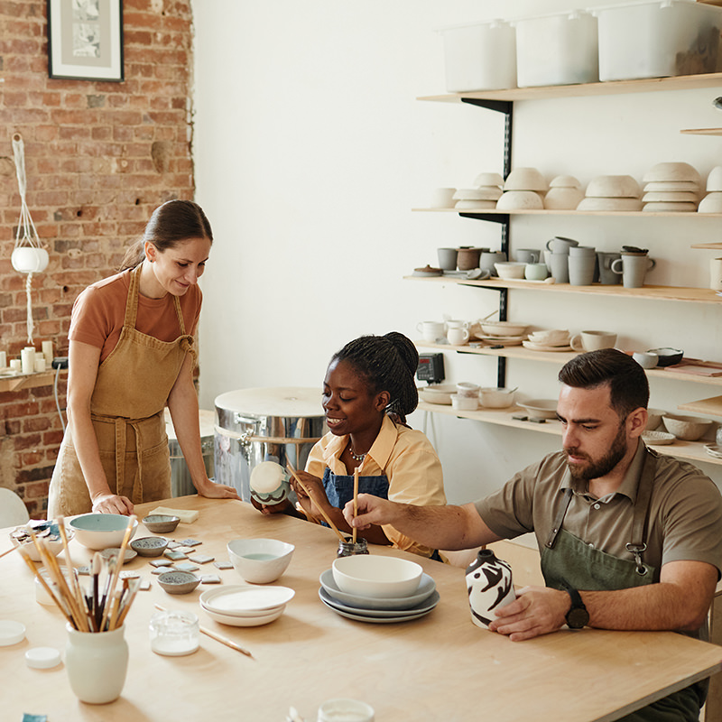 Warm toned shot of creative group of people decorating ceramics in pottery workshop.